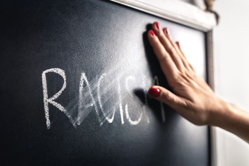 Racism concept. Stop hate and discrimination. Against prejudice and violence. Hand wiping off and erasing the word from blackboard.
