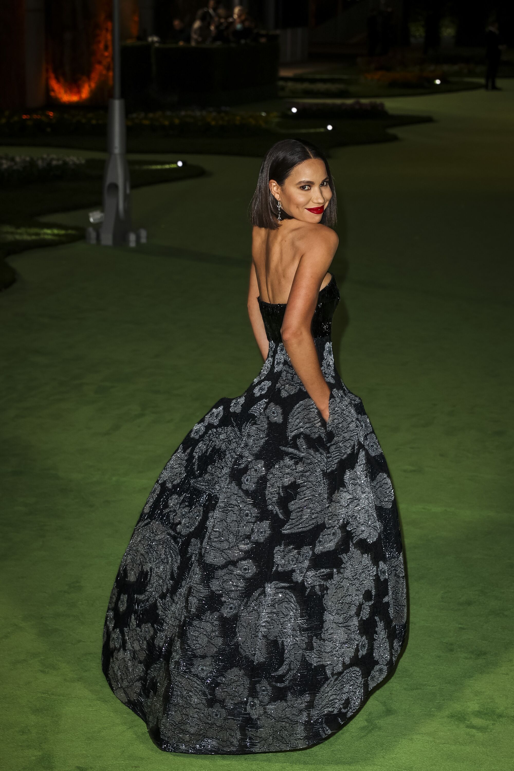 A woman in a patterned, black dress posing on a green carpet