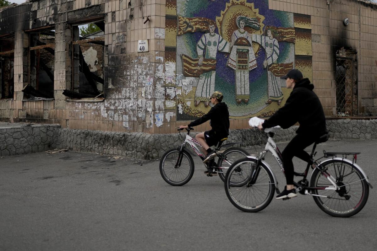 People ride bikes past a building damaged by shelling in Ukraine.