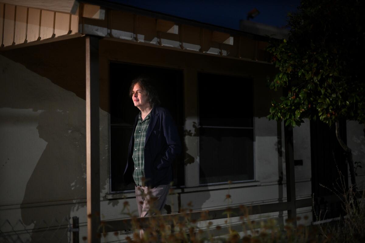 A smiling man stands outside a house