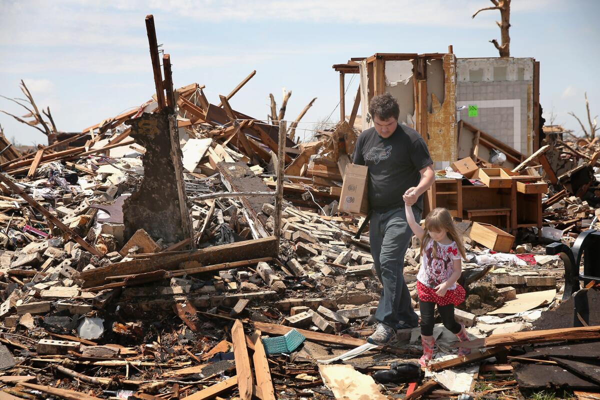 Lee Haskins leaves his house, which was destroyed by Monday's tornado, with his daughter Elizabeth Haskins, 4, after recovering a few items in Moore, Okla.