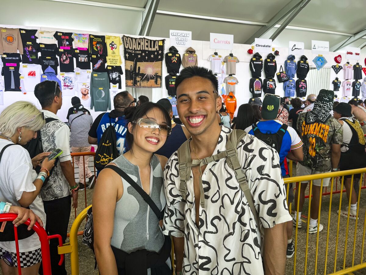 Charlize Agabon and Kaleem Syed in front of a merch table at Coachella.  