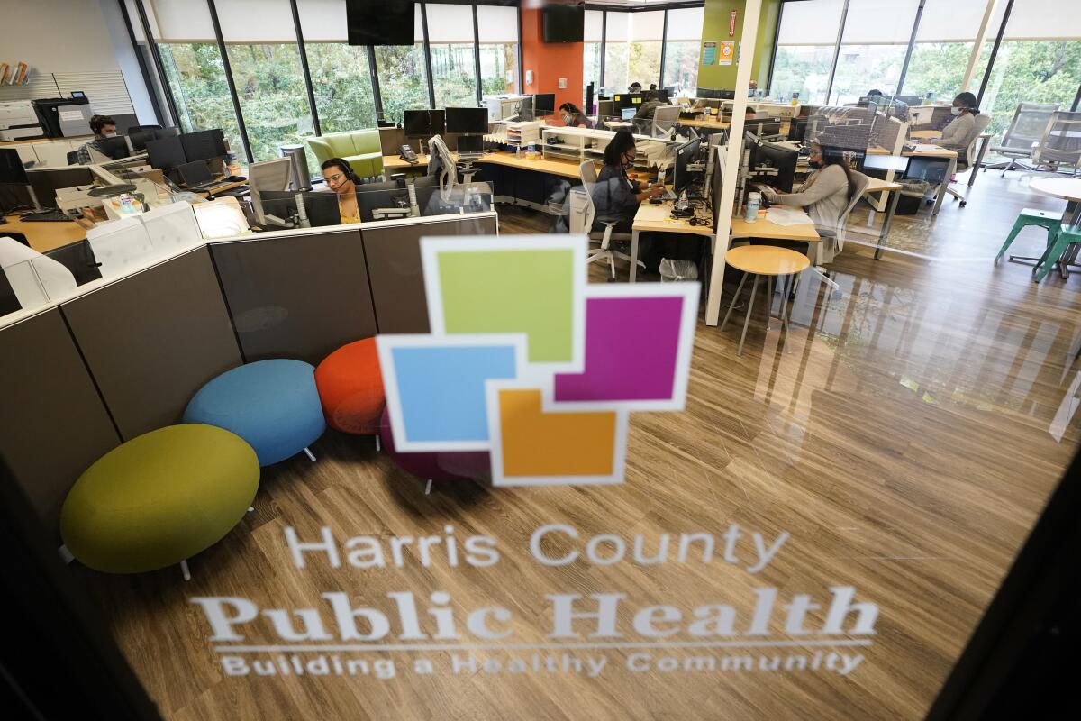 People work in an office at computers behind a logo for Harris County Public Health.