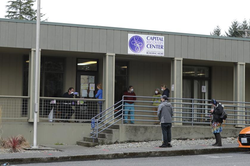 In this March 27, 2020 photo, patients line up to pick up medication for opioid addiction at a clinic in Olympia, Wash., that is currently meeting patients outdoors and offering longer prescriptions in hopes of reducing the number of visits and the risk of infection due to the outbreak of the new coronavirus. The coronavirus pandemic is challenging the millions who struggle with drug and alcohol addiction and threatening America's progress against the opioid crisis, said Dr. Caleb Alexander of Johns Hopkins' school of public health. (AP Photo/Ted S. Warren)