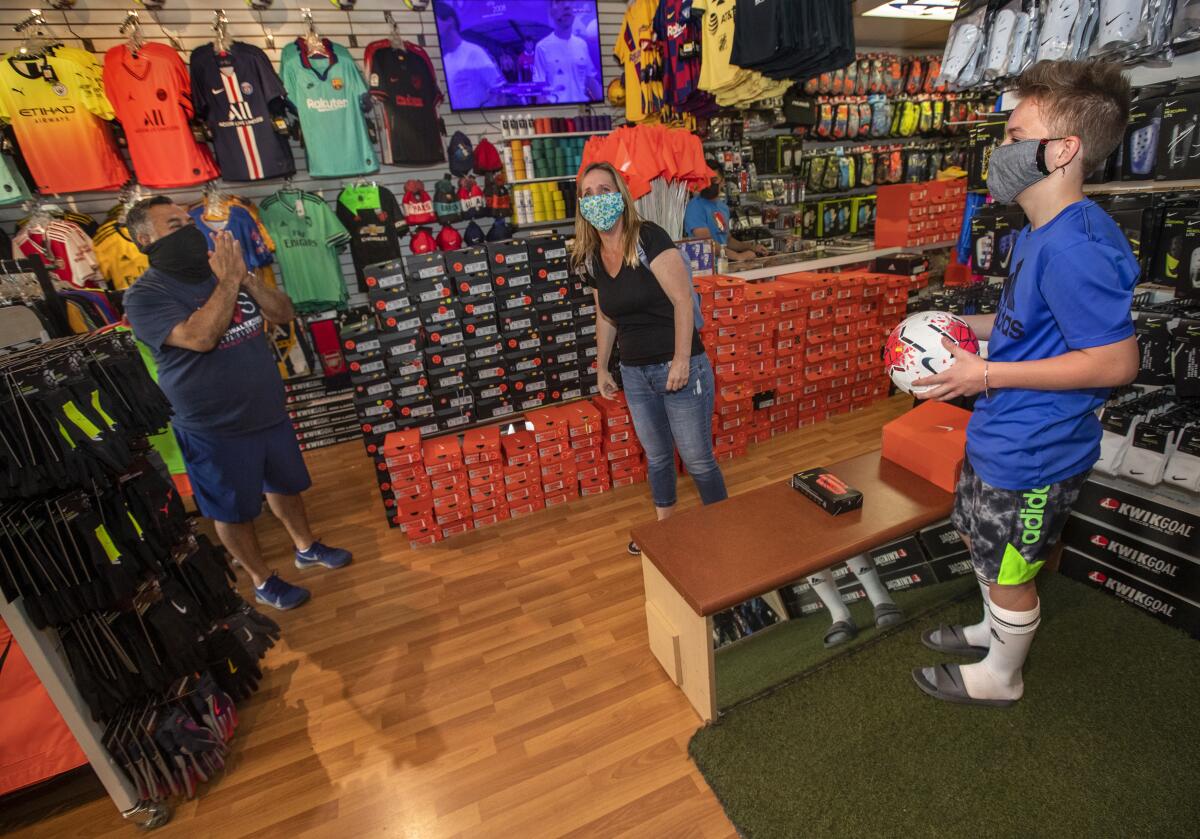 Carlos Marroquin, owner of Planet Soccer in Newhall, shows his appreciation to customers Benton Watkins and Benton’s mom, Noelle, at Marroquin’s reopened store.