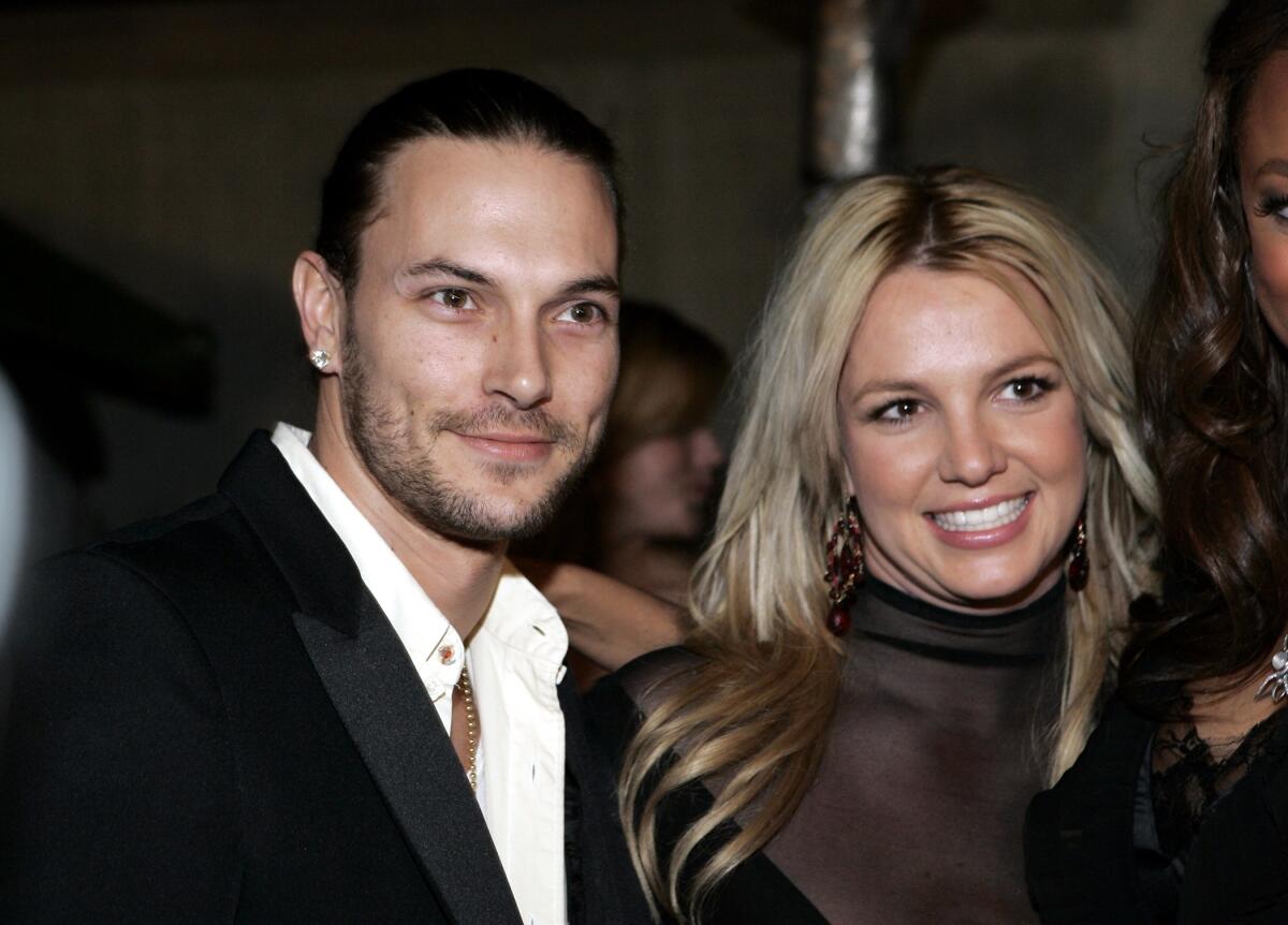 Kevin Federline wearing a white shirt and a black suit, posing next to Britney Spears who's wearing a sheer black dress