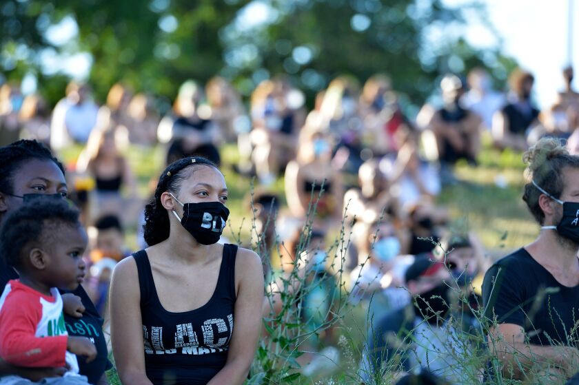 A woman wearing a "Black Lives Matter" mask and shirt listens to speakers during a Juneteenth musical rally and protest.