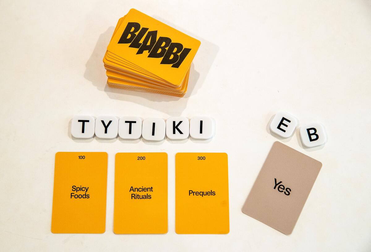 Letter tiles and cards used to play the game Blabbi sit on a white table.