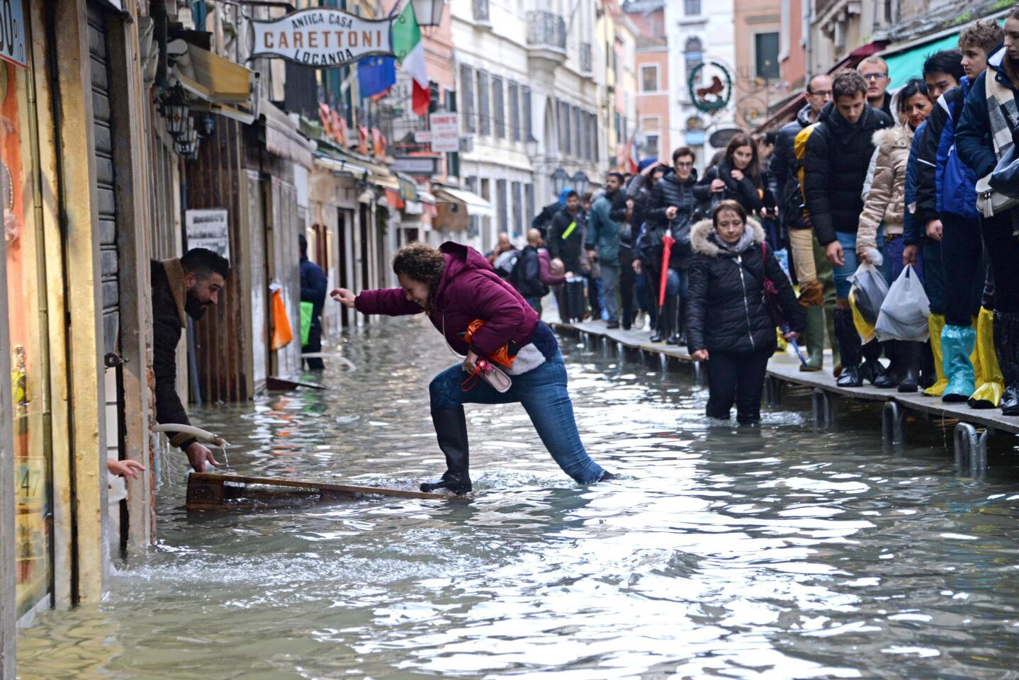 A woman tries to cross a flooded street as people walk on a trestle bridge during high water in Venice.