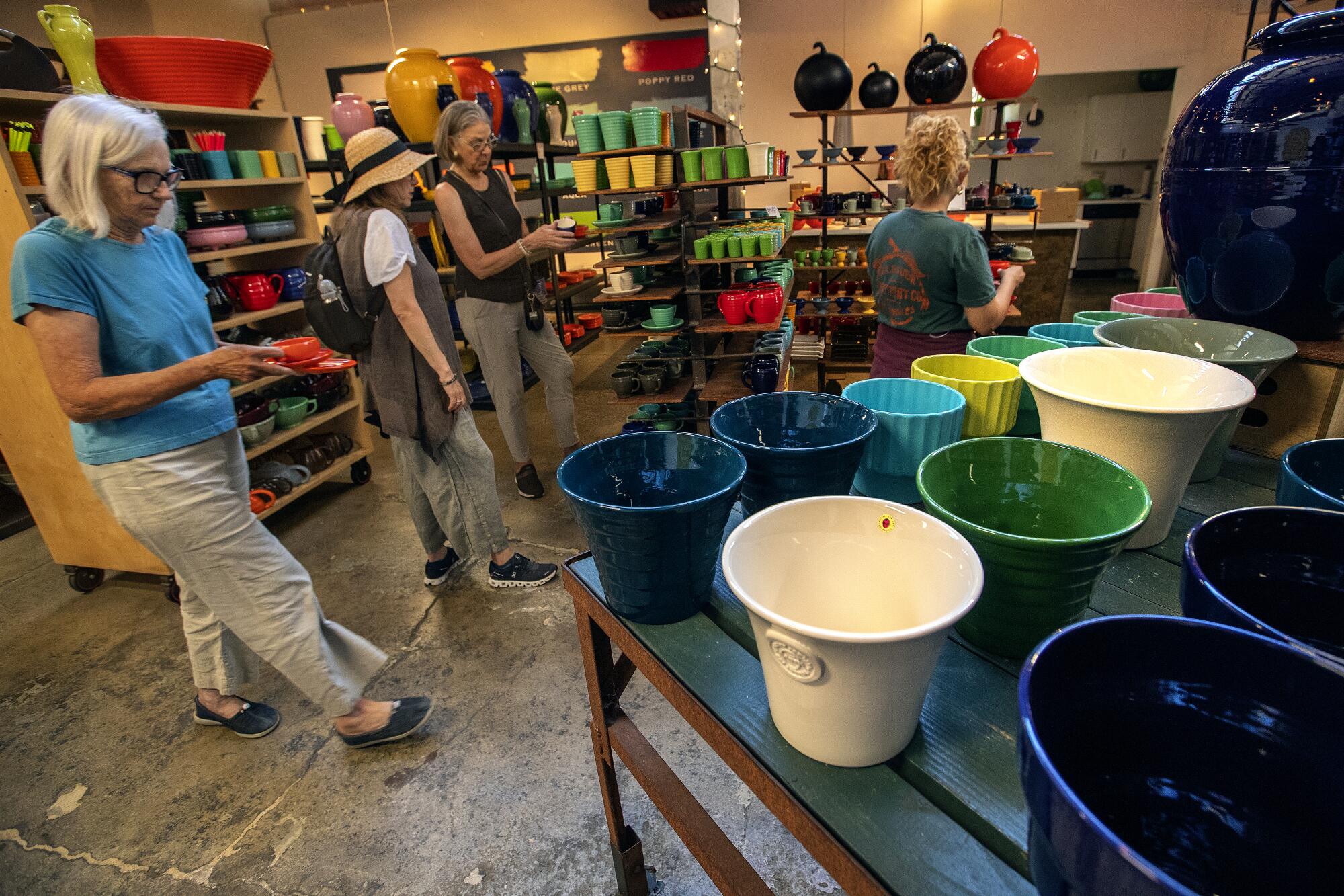 Three women browse a shop with colorful pottery