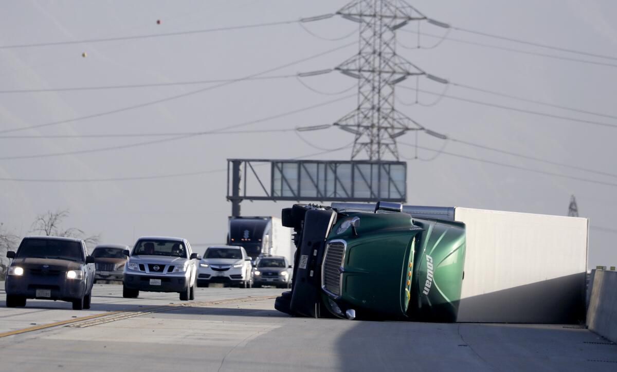 A truck lies on its side after being overturned by high winds on the southbound 15 Freeway near Duncan Canyon Road on Tuesday morning in Fontana.