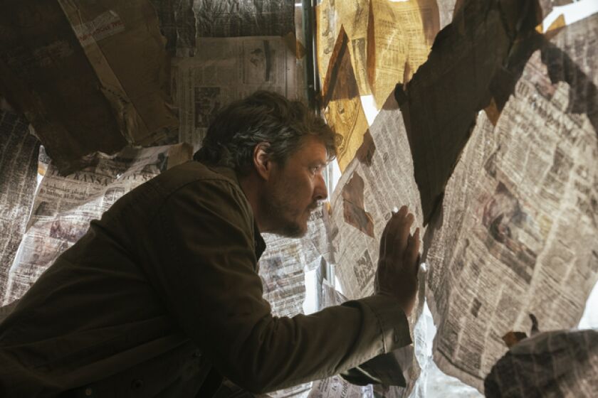 A man peers through a hole in a wall covered with newspapers.