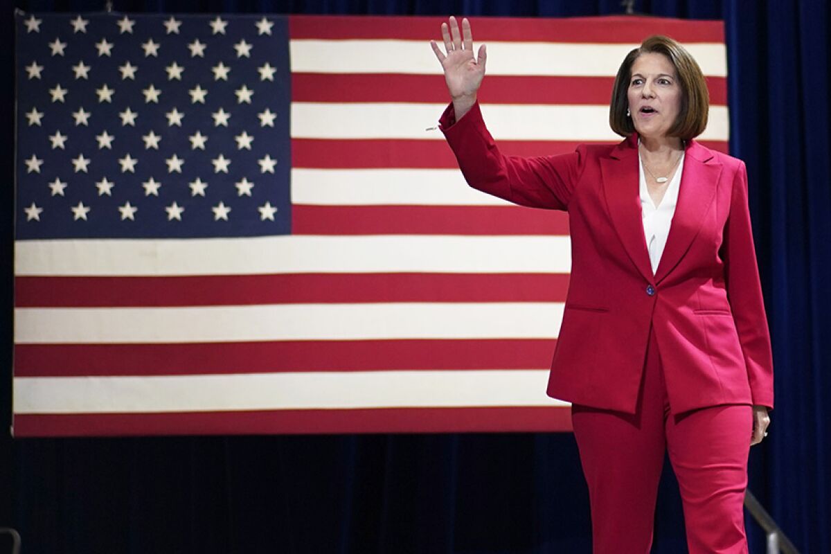 Sen. Catherine Cortez Masto waves at a rally in Las Vegas in front of a large American flag. 
