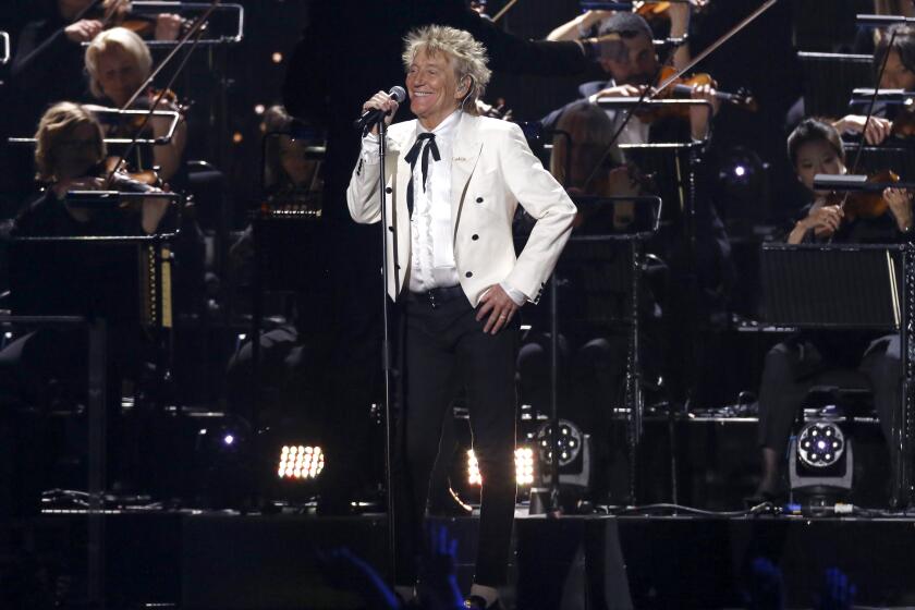Rod Stewart performs onstage in a white jacket and black pants