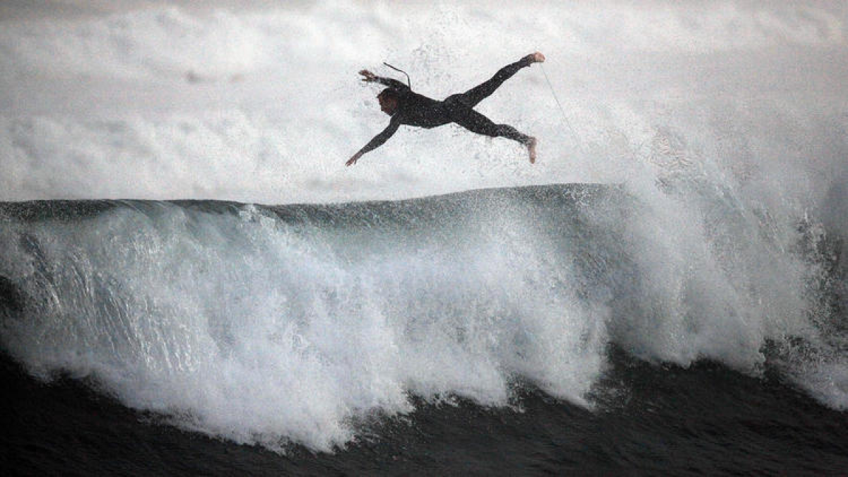 A surfer flies through the air as he punches out of one of the large storm-generated waves rolling through Southland beaches.