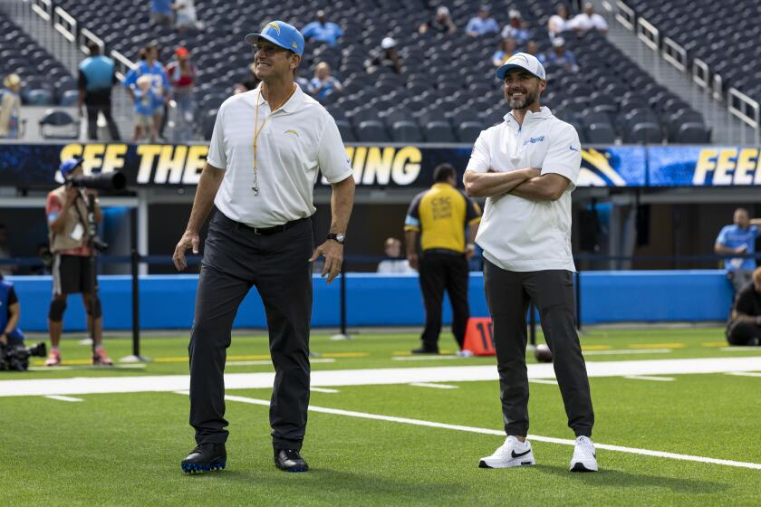 Chargers coach Jim Harbaugh and defensive coordinator Jesse Minter stand on the field before a game.