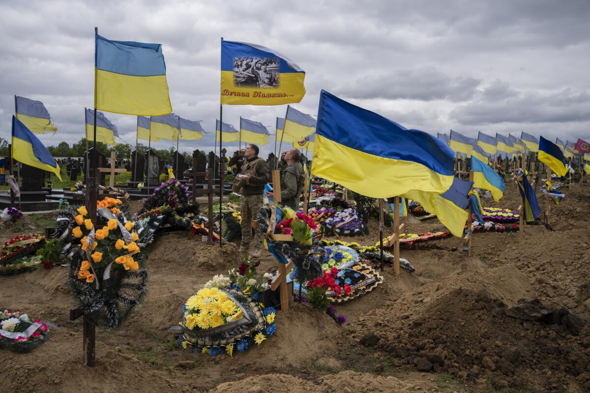 Two men stand near Ukrainian flags flying at a cemetery in Kharkiv