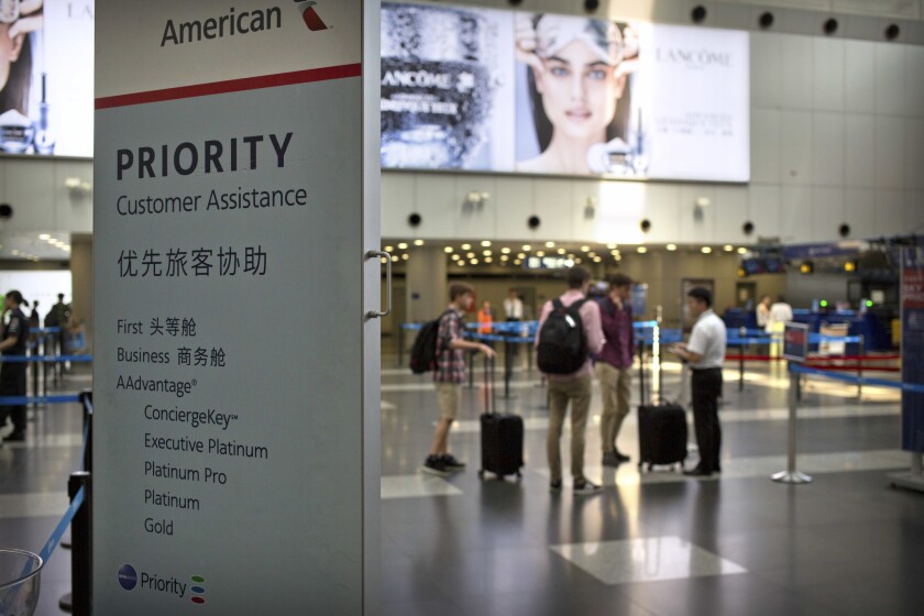 In this July 6, 2018, file photo, travelers stand near a signboard at the American Airlines check-in counters at the Beijing Capital International Airport in Beijing. Chinese regulators appear to have rejected a possible attempt by U.S. airlines at a compromise over Beijing's demand to call self-ruled Taiwan a part of China, an order Washington opposed.
