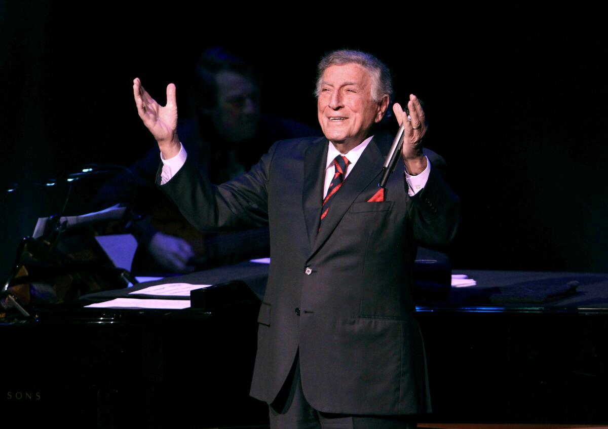 Tony Bennett performs on stage with his arms raised and smiling.