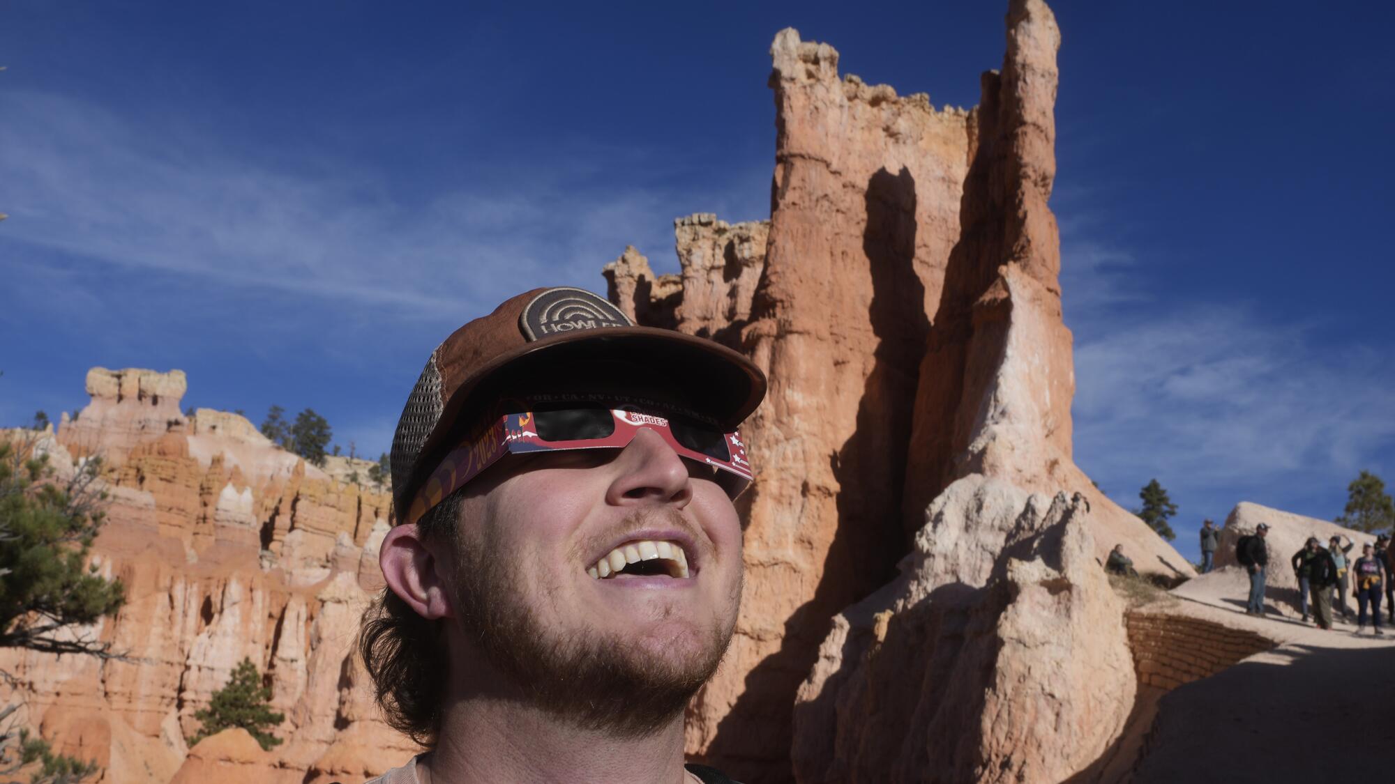A person wearing special glasses watched an eclipse while standing in front of rock formations.