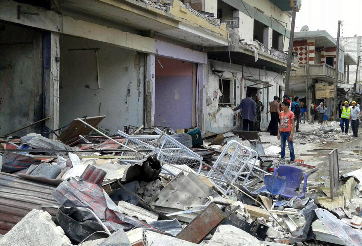 Fotografía difundida por la agencia noticiosa oficial siria SANA, de varios residentes en el sitio de dos atentados explosivos en Mukharam al-Fawkani, al este de la ciudad siria de Homs. (SANA vía AP)