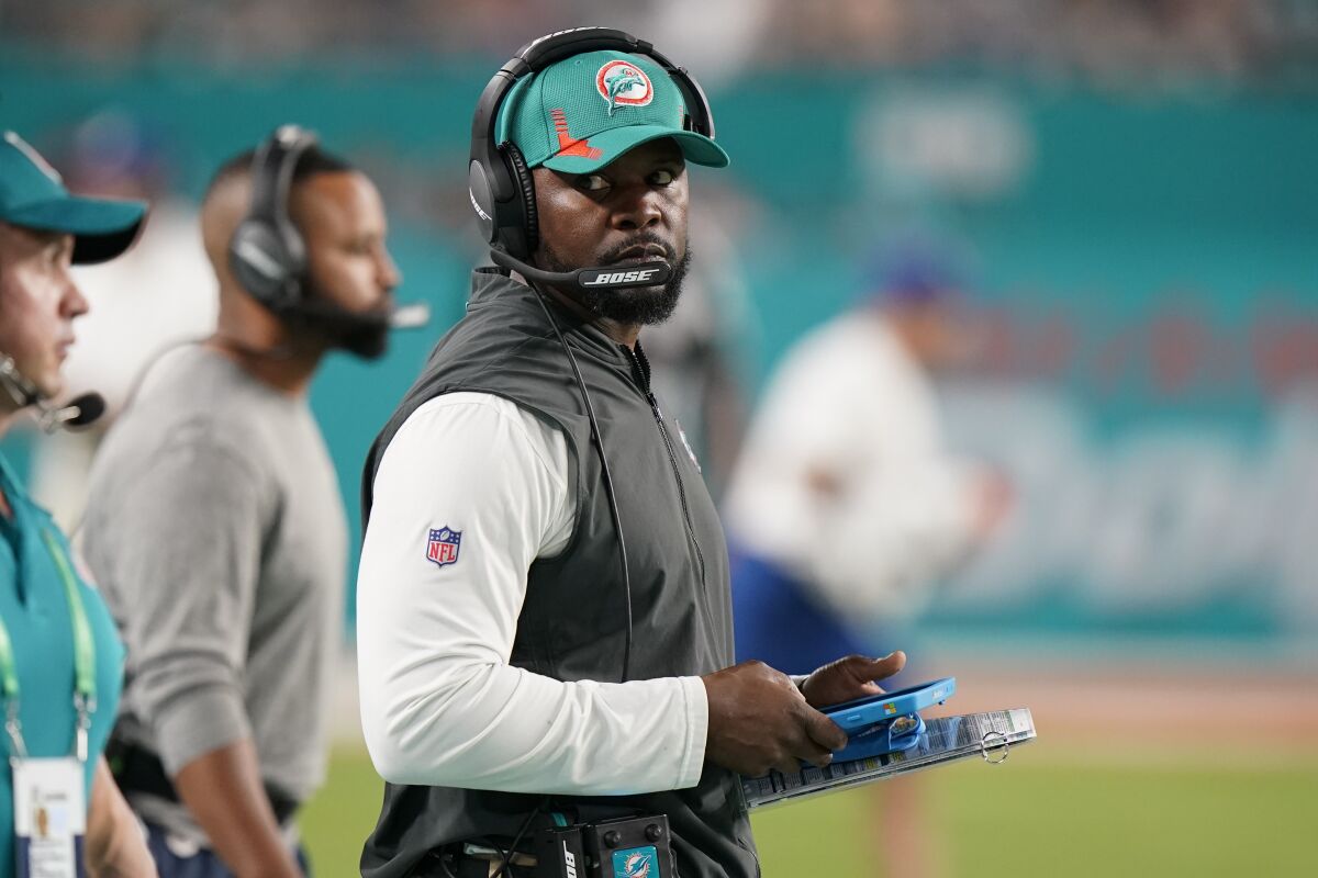 Miami Dolphins head coach Brian Flores glances to the side while holding a clipboard on the sideline.