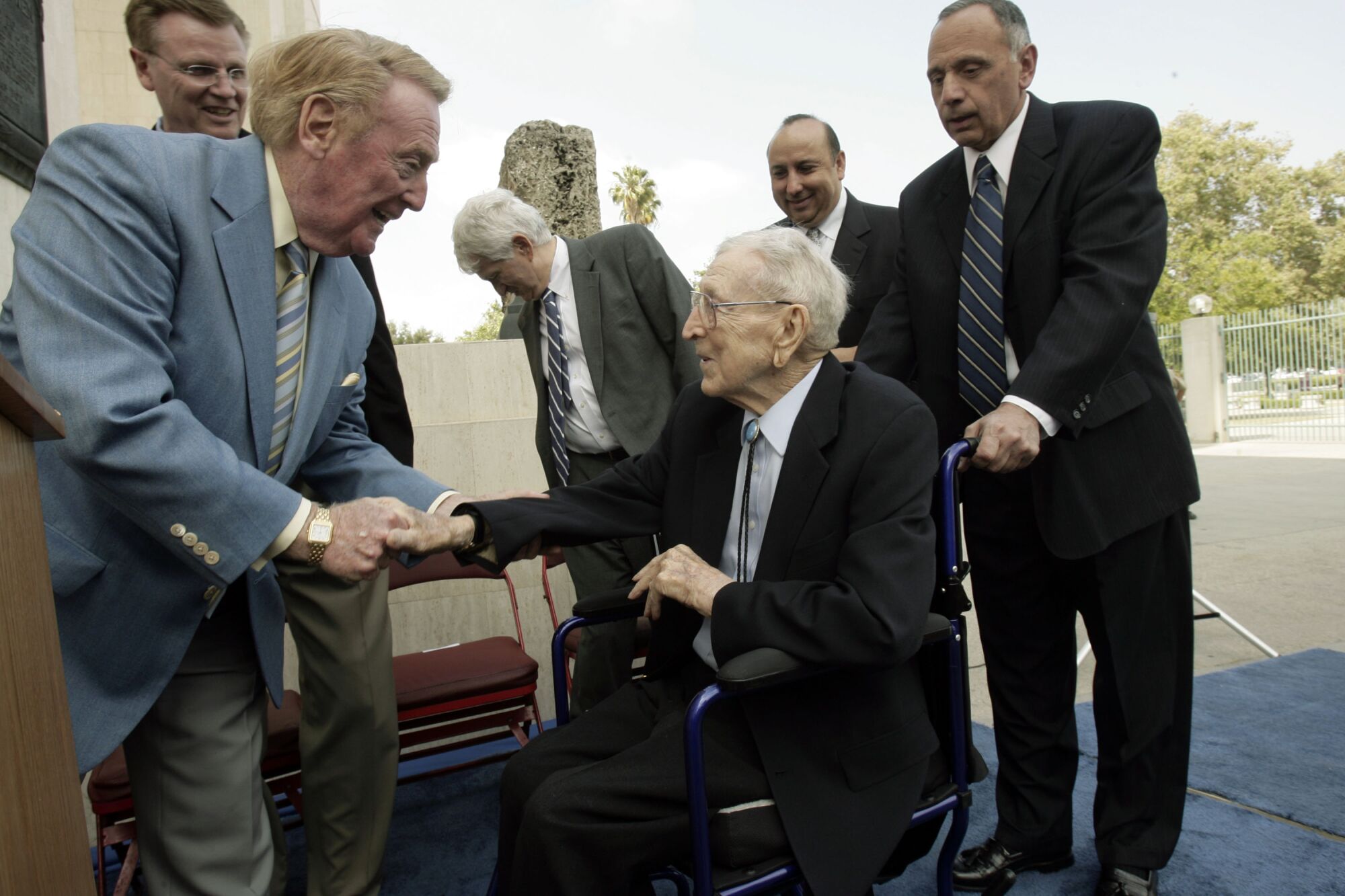 Former UCLA basketball coach John Wooden, center, is greeted by sportscaster Vin Scully at the Los Angeles Coliseum.