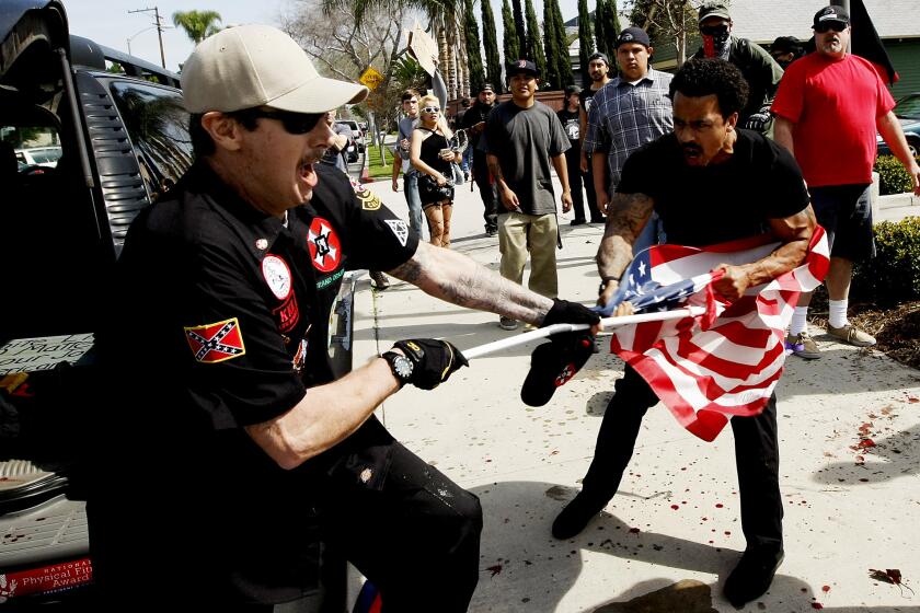 A Ku Klux Klansman, left, struggles with a protester for an American flag after members of the KKK tried to start a "White Lives Matter" rally at Pearson Park in Anaheim on Saturday. Three people were treated at the scene for stab wounds, and 13 people were arrested.