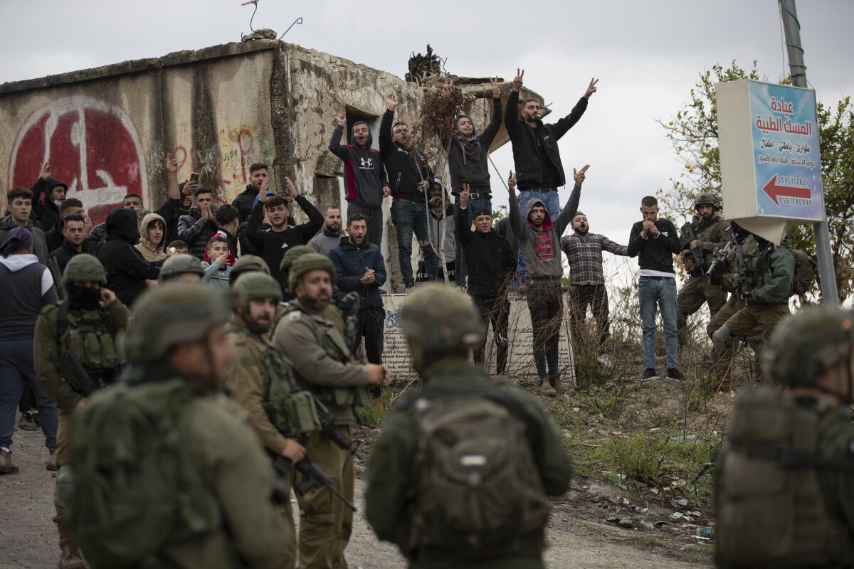 Israeli soldiers stand between Palestinians and a Jewish settler following a settler attack on the West Bank village of Burqa, Friday, Dec. 17, 2021. Palestinian officials said at least two people have been injured in a string of Jewish settler attacks in northern West Bank villages, a day after an Israeli settler was shot dead by Palestinian gunmen. (AP Photo/Majdi Mohammed)