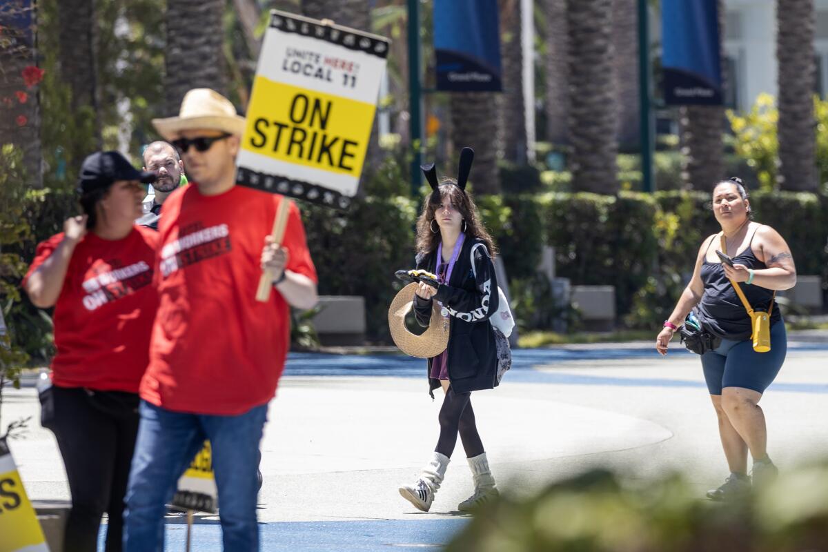 After exiting the Hilton Anaheim tourists walk near striking hotel workers 