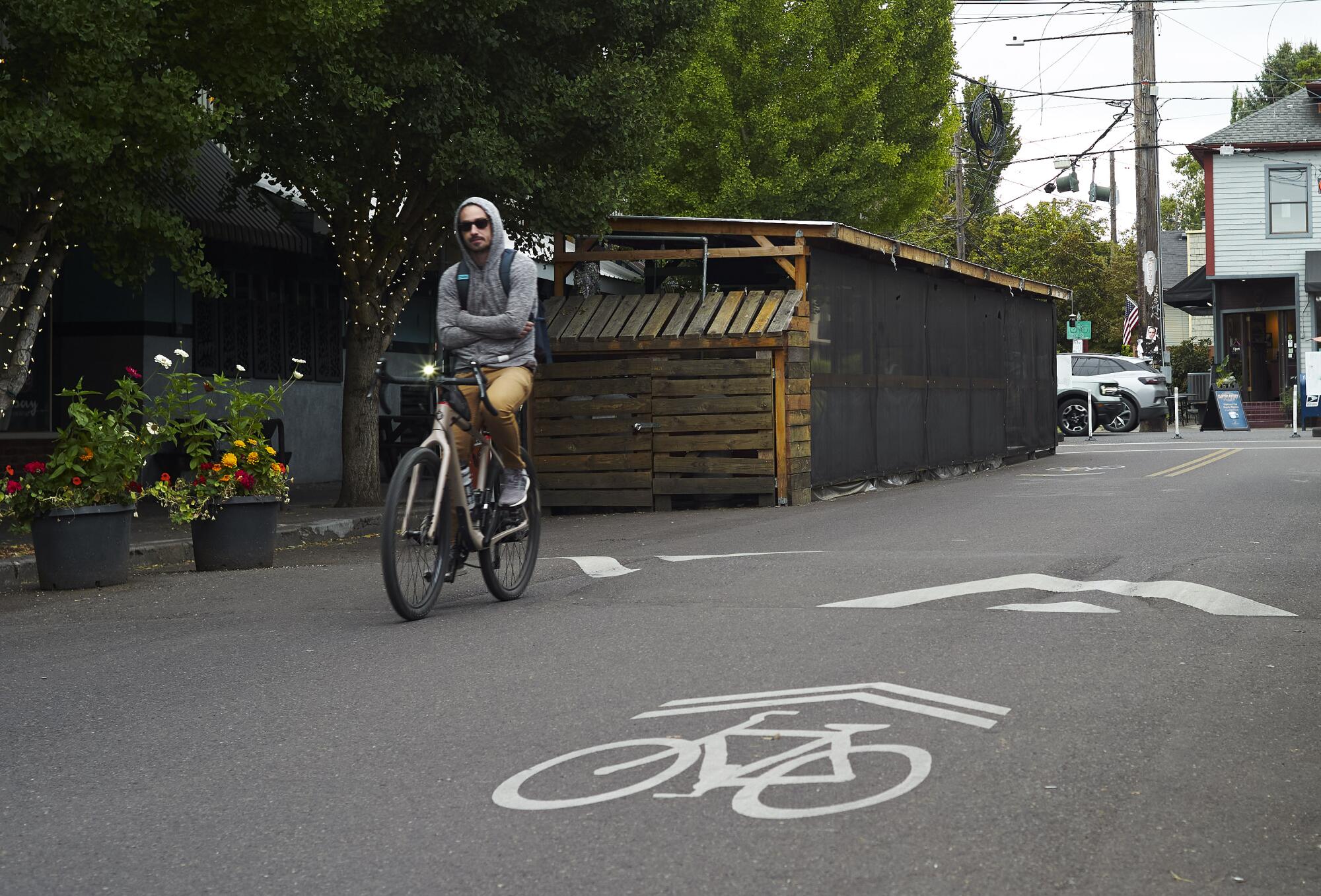 A cyclist rides no-handed on a tree-lined city street. 