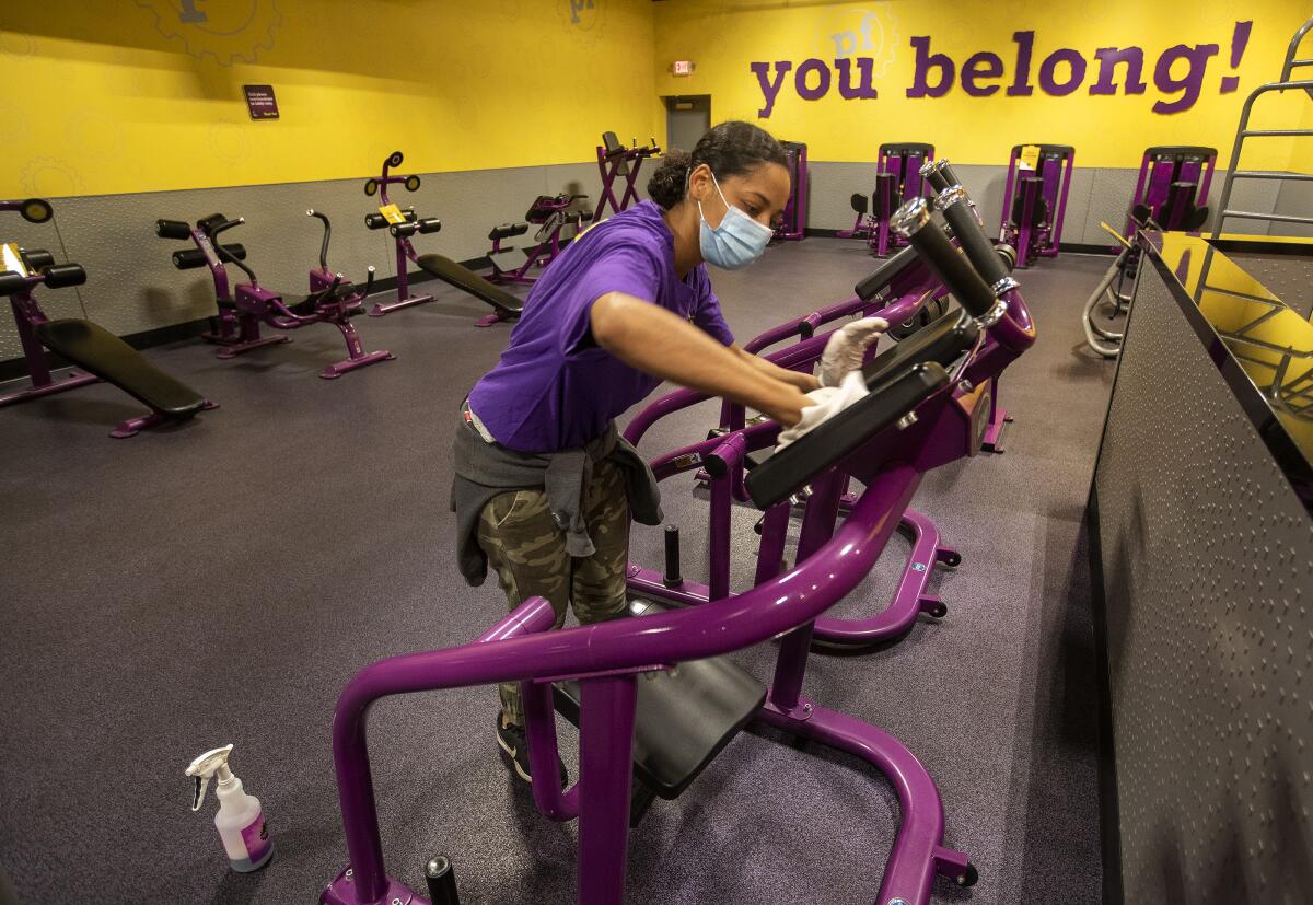 A mask-wearing woman wipes down gym equipment.