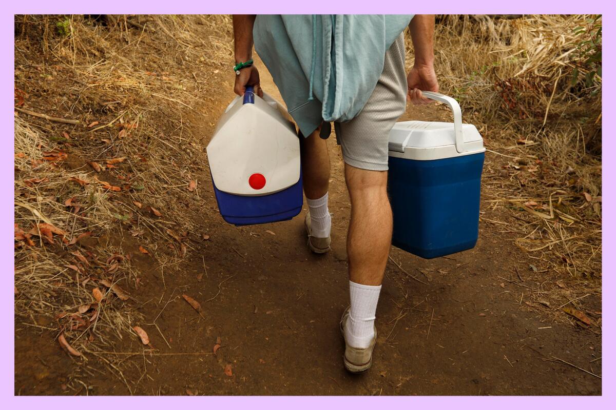 A person carries coolers filled with drinks that will be given to hikers along a trail.