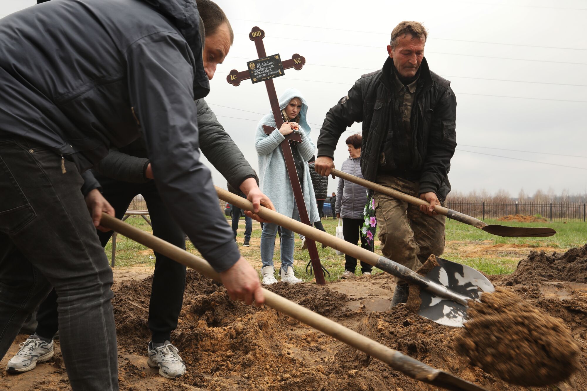 A year of war: Los Angeles Times photographers document the battle in Ukraine 17 Men with shovels dig as a woman holding a larger cross stands nearby