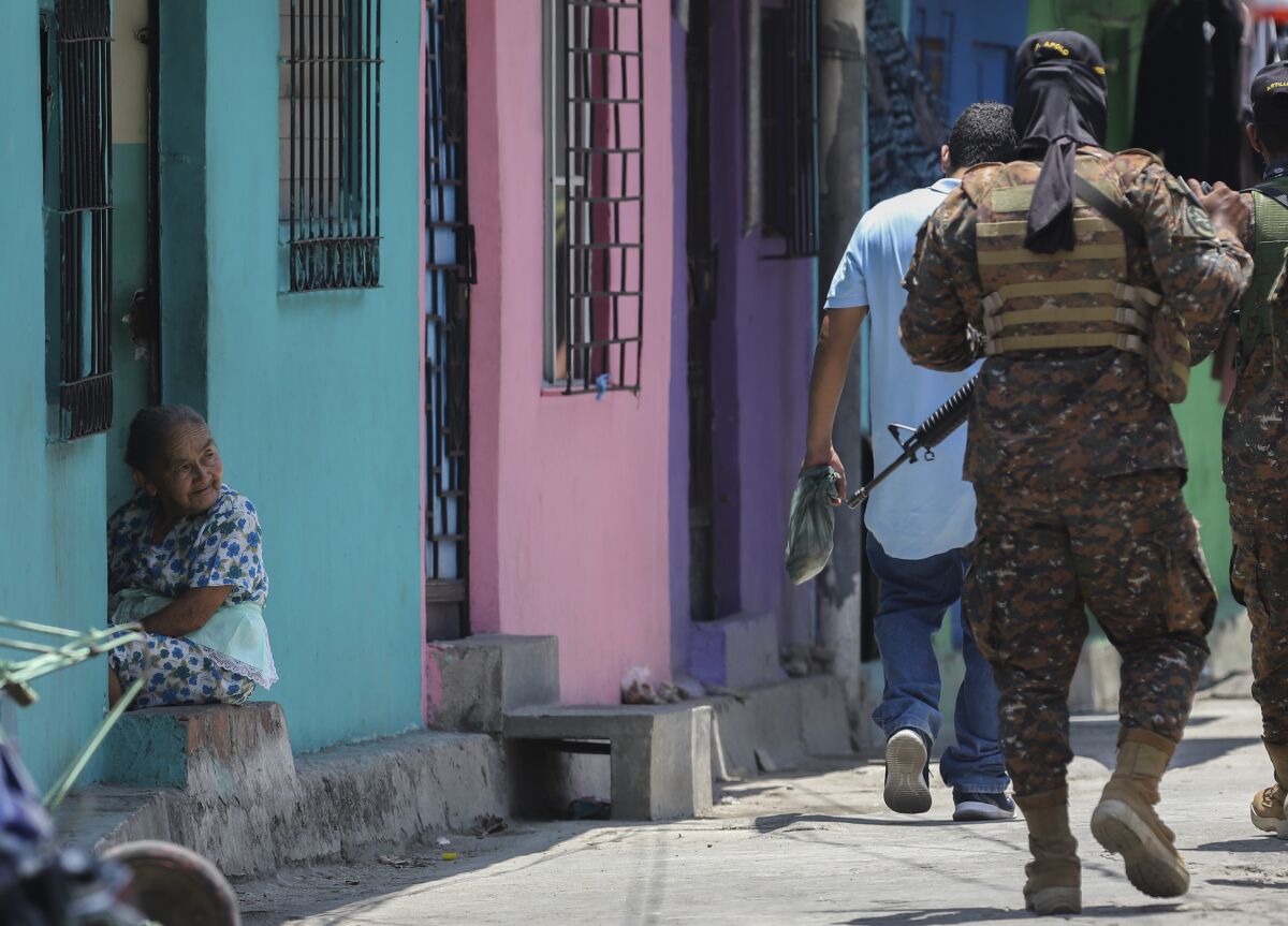 An elderly woman watches as soldiers patrol in the San Jose del Pino Community in Santa Tecla, El Salvador, Wednesday, April 6, 2022, during the government's unprecedented crackdown on gangs. El Salvador's congress, pushing further in the government's crackdown, has authorized prison sentences of 10 to 15 years for news media that reproduce or disseminate messages from the gangs, alarming press freedom groups. (AP Photo/Salvador Melendez)