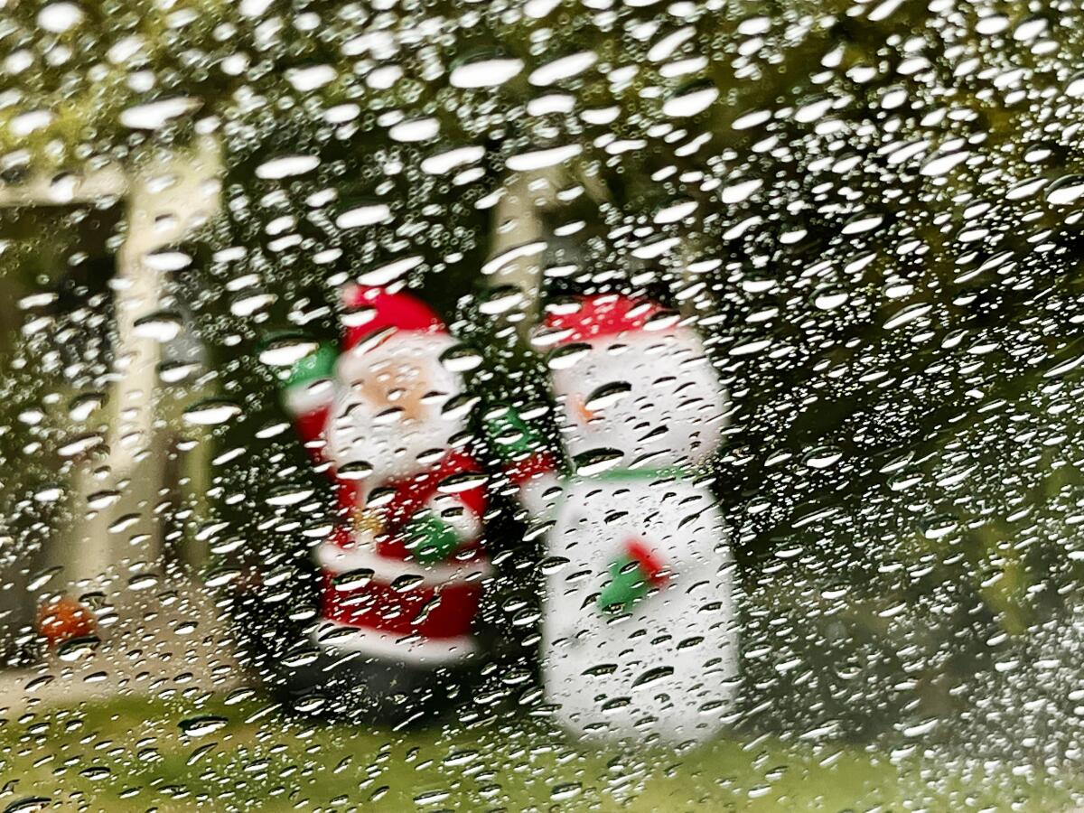 Raindrops on a windshield obscure Christmas decorations.