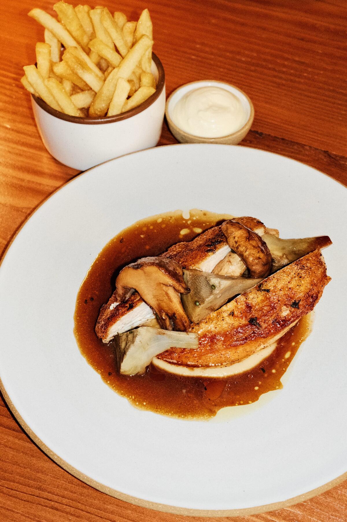 Roast chicken with foraged mushrooms, jus, frites and garlic aioli on wood table at Long Beach restaurant Olive & Rose