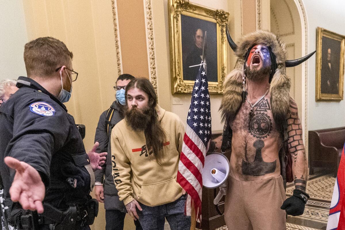 Men, including one wearing a fur hat with horns, are confronted by U.S. Capitol Police officers outside the Senate Chamber.