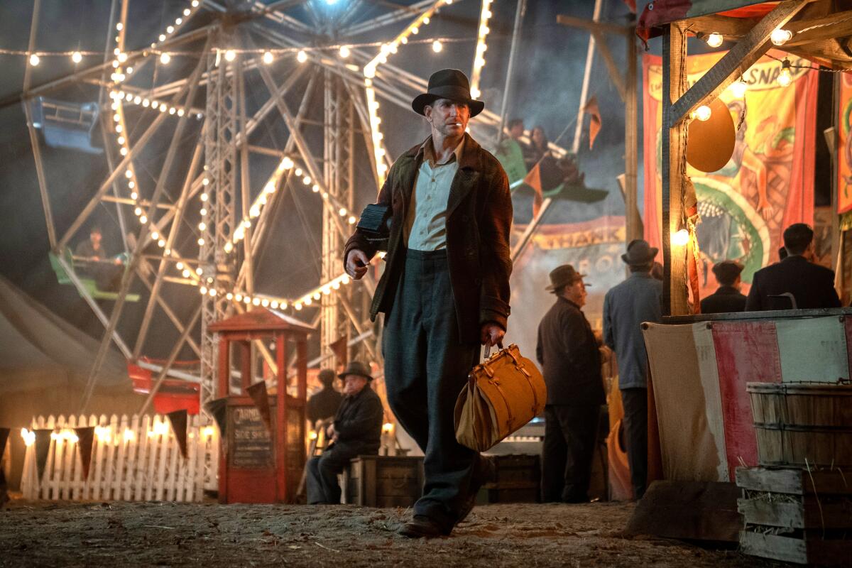 Bradley Cooper walks past the lights of the Ferris wheel in 'Nightmare Alley.'