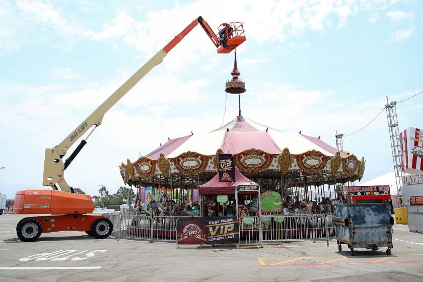 A Ray Cammack Shows, Inc. (RCS) crane lowers the spire on a centerpeice carousel ride as vendors, ride operators and concessionaires assemble and prepare for the 2024 Orange County Fair "Always a Good Time" theme in Costa Mesa on Thursday.