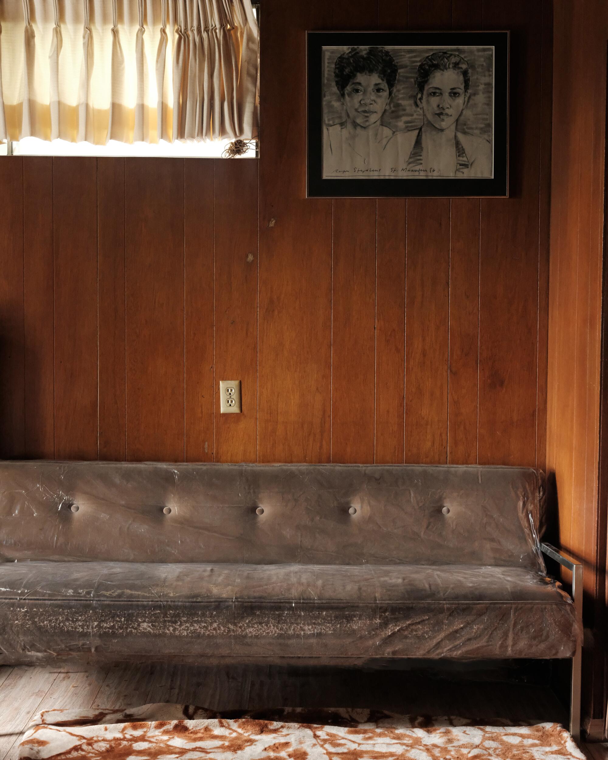 A photo of a brown plastic-covered couch, a portrait of two women hanging above it.