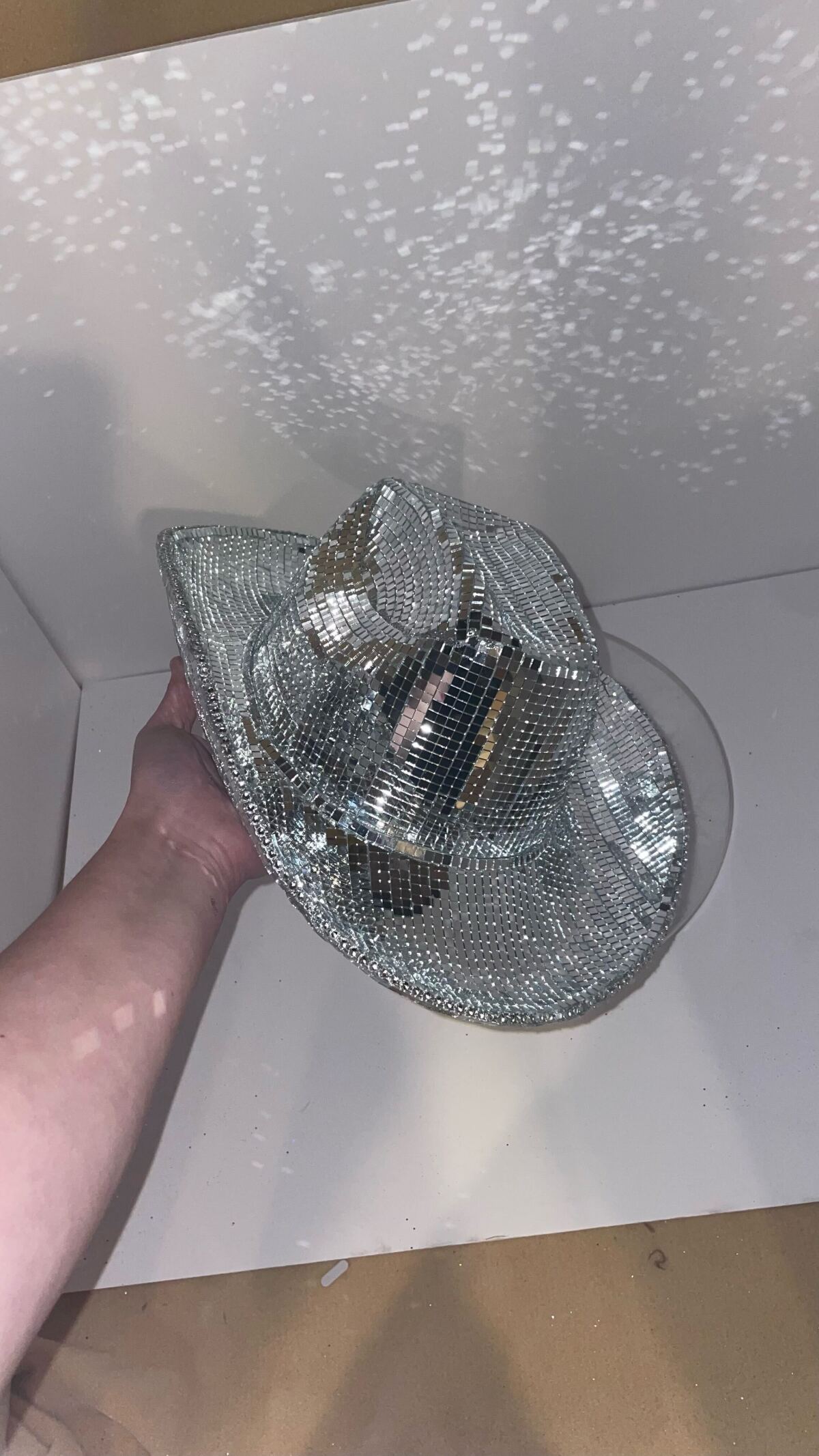 A cowboy hat covered in disco balls held up to the ceiling with light refracting off the walls