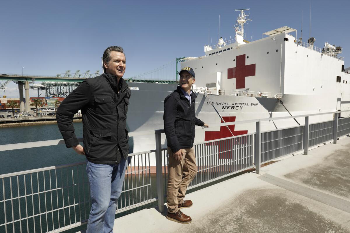 Gov. Gavin Newsom, left, and Los Angeles Mayor Eric Garcetti, stand in front of the hospital ship USNS Mercy that arrived into the Port of Los Angeles on Friday. Both Newsom and Garcetti have announced a delay on evictions for tenants who cannot pay their rent because of the pandemic outbreak.