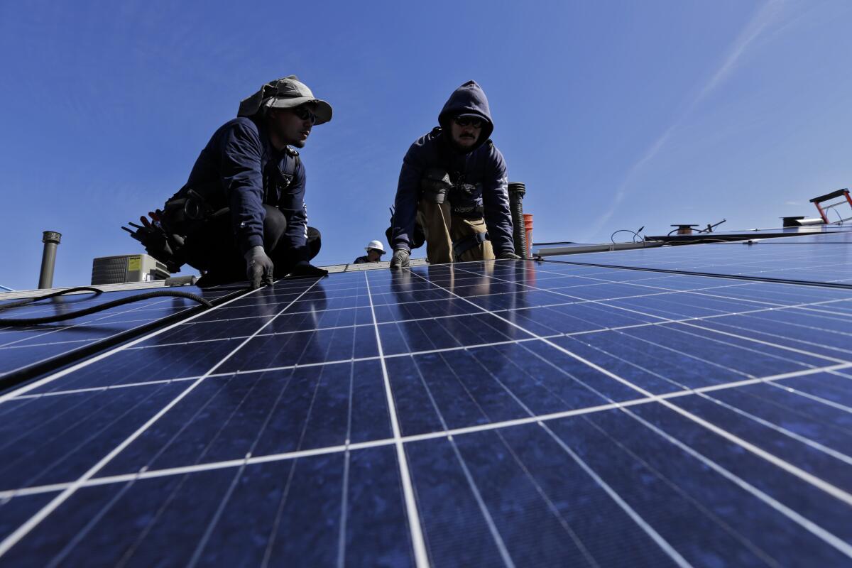 Two men kneel while working on solar panels outdoors.