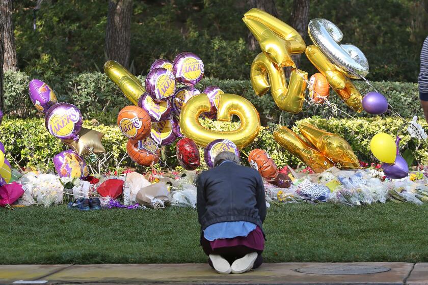 A woman prays Monday at a makeshift memorial for Lakers legend Kobe Bryant outside Pelican Crest, the gated community in Newport Coast where Bryant lived with his family. His daughter Gianna, 13, died with him Sunday in a helicopter crash in Calabasas.