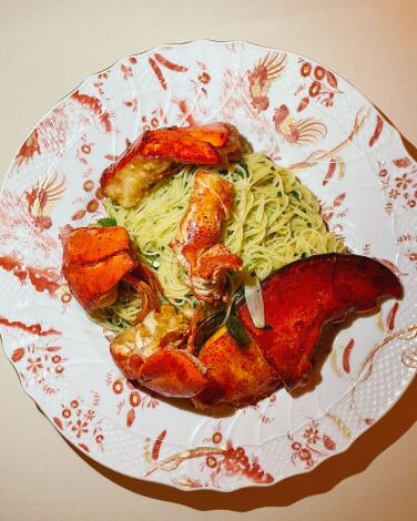 An overhead photo of Torrisi's Capellini Cantonese: whole lobster claw and morsels sit atop pasta on a patterned  plate.