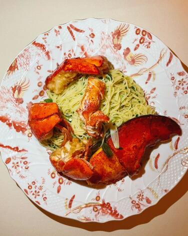 An overhead photo of Torrisi's Capellini Cantonese: whole lobster claw and morsels sit atop pasta on a patterned plate.
