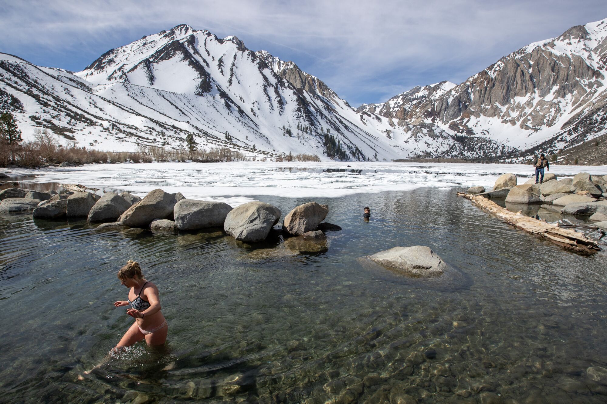 A swimmer quickly moves out of a frigid lake with snow and ice in the background.