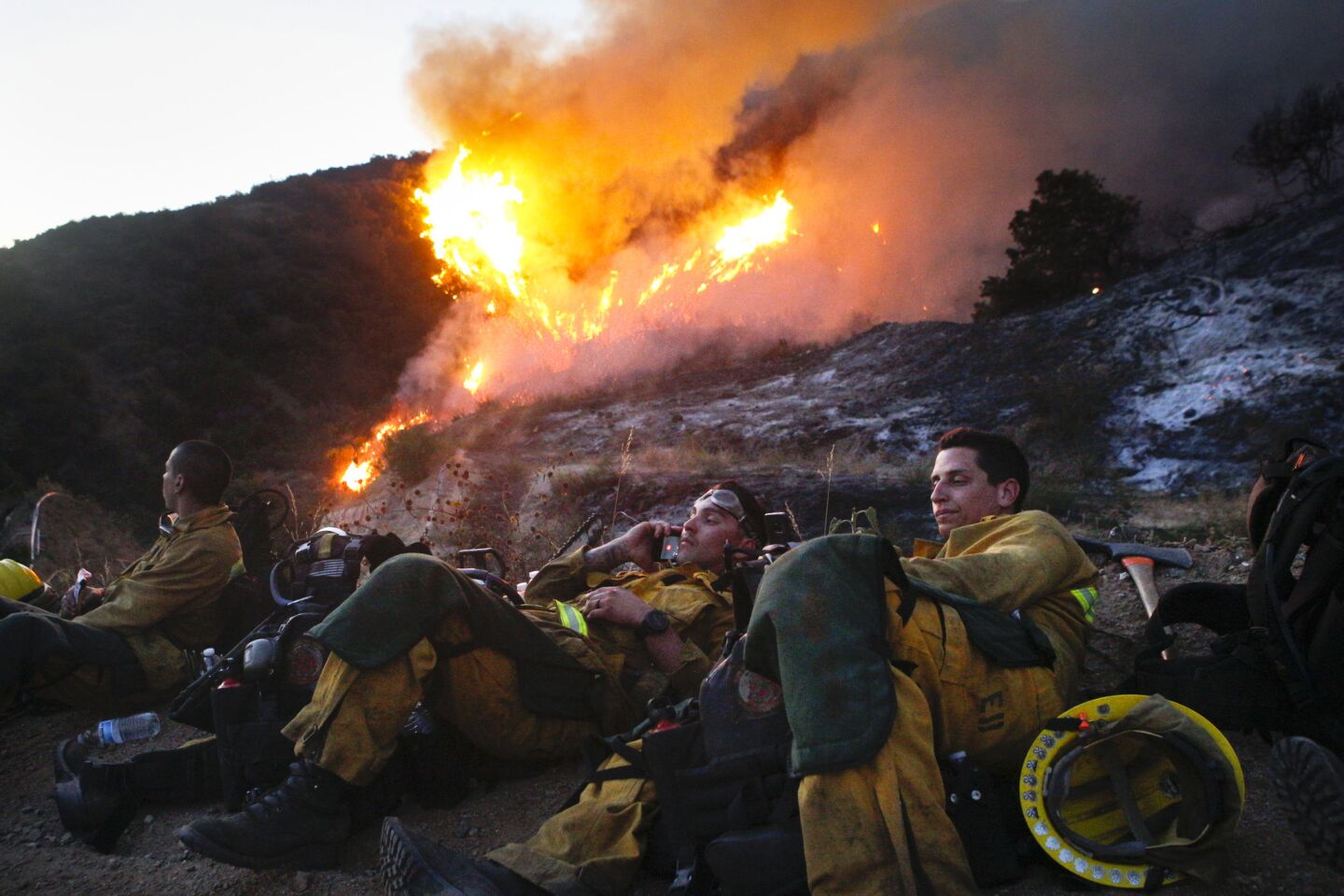 Los Angeles County firefighters rest as the Fish Fire burns behind them Monday afternoo in Duarte.