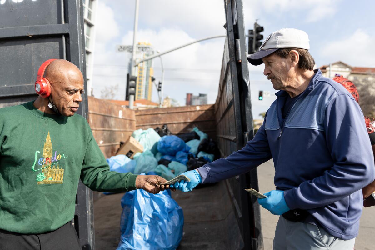 Retired attorney Brian Trotier (right) gives cash to homeless man for picking up trash in downtown San Diego.